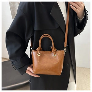 Caramel brown leather tote bag with thin shoulder strap worn over a black winter coat