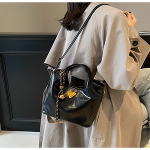 Détail du sac à main noir verni avec logo triangulaire doré et pendentif tressé élégant