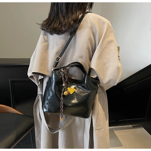 Détail du sac cabas en cuir verni noir avec logo triangle jaune et pendentif tressé