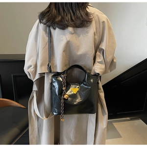 Détail du sac fourre-tout noir brillant avec logo triangle jaune et pendentif tressé