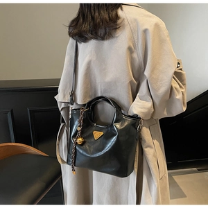 Détail du sac cabas en cuir noir brillant avec breloque cloche dorée et logo sur un trench