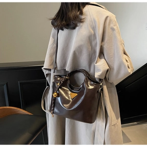 Détail d'un sac cabas marron foncé en cuir brillant avec logo triangulaire doré