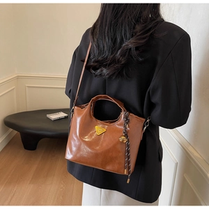 Détail du sac à main en cuir marron avec logo triangulaire et breloque tressée