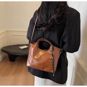 Vue latérale du sac en cuir marron caramel avec logo triangulaire et charm tressé