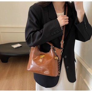 Détail d'un sac seau en cuir marron avec logo triangle doré et charm de cloche