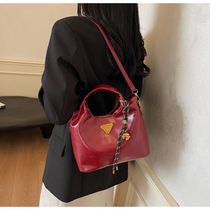 Détail du sac en cuir bordeaux avec logo triangulaire doré et charm clochette tressé