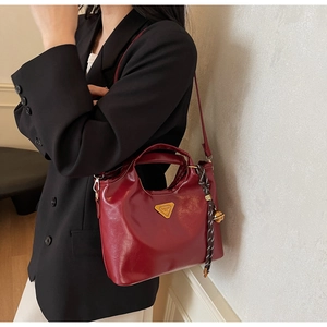 Détail d'un sac cabas rouge foncé brillant avec emblème doré et pendentif en corde tressée