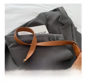 Detail of brown lychee leather shoulder bag with wide comfortable strap on grey blazer