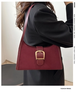 Detail of burgundy suede shoulder bag with gold square buckle worn over a black blazer