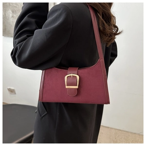 Detail of burgundy suede shoulder bag with wide strap and large gold metal buckle