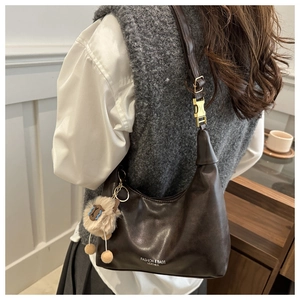 Detail of dark brown leather handbag with gold buckle and plush animal charm on model