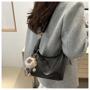 Detail of black leather hobo bag with fashion logo and plush charm worn by model