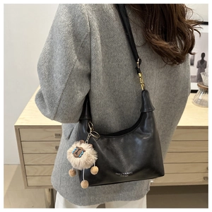 Detail of black leather hobo bag with gold hardware and a cute beige plush charm