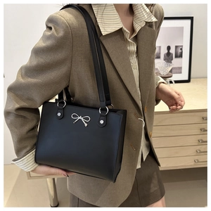 Elegant black leather tote bag with silver butterfly buckle worn by a model in a modern room