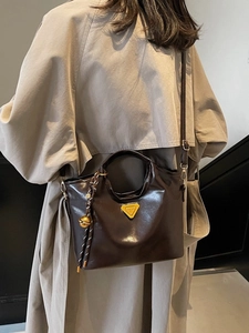 Sac cabas en cuir marron avec logo doré et bijou de sac porté sur un trench-coat beige