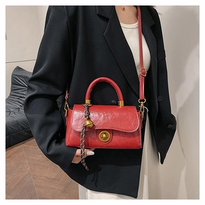 Détail du sac à bandoulière en cuir rouge avec texture vintage et breloque cloche
