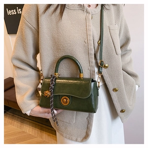 Détail d'un sac rétro en cuir vert foncé avec boucle dorée et accessoire décoratif