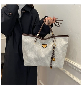 Détail du grand sac cabas gris avec bordure marron et emblème triangulaire en métal