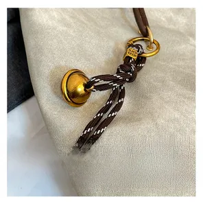 Détail du cordon bicolore avec cloche en laiton et boucle métallique dorée gravée