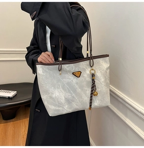 Vue détaillée du sac cabas gris avec garniture en cuir et logo triangulaire tenu par un mannequin