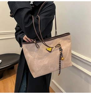 Détail du grand sac cabas beige avec anses marron et breloque porté sur un manteau noir