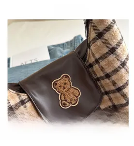 Gros plan du sac en tissu écossais marron et cuir avec broderie d'ours en peluche