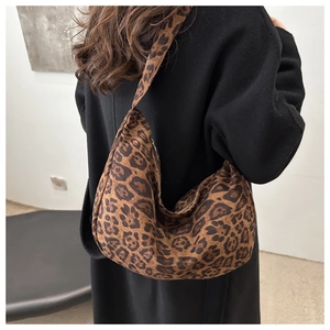 Detail of large leopard print hobo bag with black strap worn over a black winter coat
