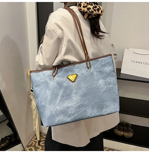 Détail du grand sac cabas en denim bleu avec anses brunes et logo triangle jaune
