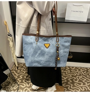 Détail du sac cabas bleu motif nuage avec anses en cuir marron et breloque dorée