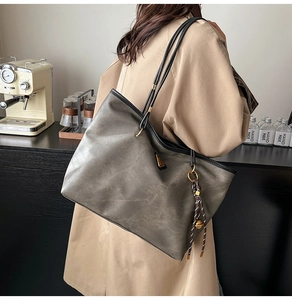 Détail d'un sac cabas vintage gris-vert foncé avec texture cuir et accessoire à pompon
