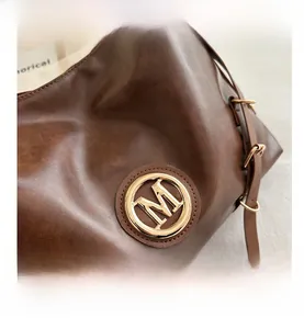 Detail of gold metal M logo and side buckle on dark brown leather tote handbag