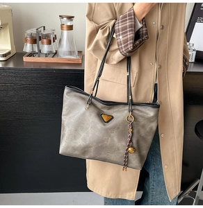 Détail du sac cabas en cuir gris vintage avec breloque tressée sur la bandoulière