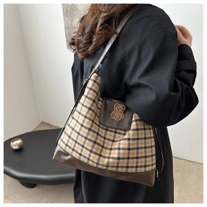 Détail d'un sac cabas à carreaux avec finitions en cuir et poche ornée d'un ours en 3D
