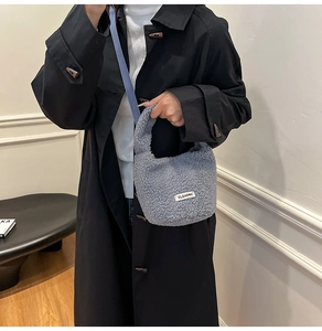 Detail of grey fuzzy plush handbag with brand tag held by model in autumn outfit