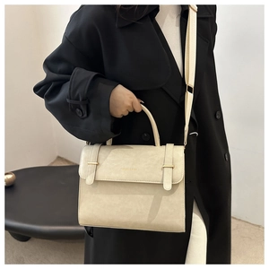 Détail d'un sac bandoulière beige en similicuir avec boucle dorée et sangle tissée