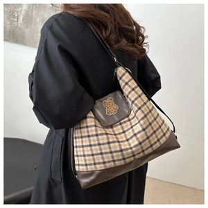 Detail view of a plaid tote bag with brown bear embroidery on a black coat model