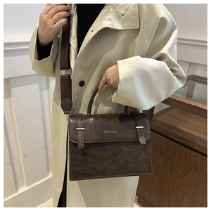 Détail du sac à main en cuir marron foncé avec boucles dorées et bandoulière textile