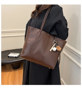 Detail view of coffee brown tote bag in glossy faux leather with baseball pendant