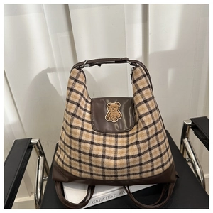 Close-up of retro plaid backpack featuring a brown leather flap and cute teddy bear patch