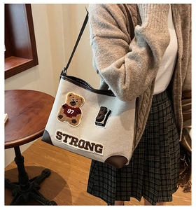Close-up of canvas tote featuring plush bear patch and embroidered strong text detail