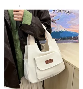 Detail of white nylon tote bag featuring brown leather fashion label and front pocket