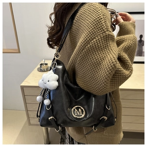 Detail of black tote bag with gold M logo and soft white plush cloud charm on a model