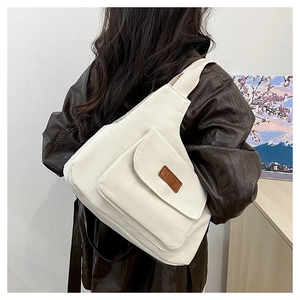 Détail du sac bandoulière en toile beige avec étiquette en cuir et poche frontale
