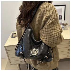 Detail of a black leather hobo bag with metal M-logo and adjustable side hardware details