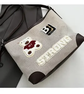 Detail of woven canvas tote with leather trim, teddy bear patch and varsity embroidery