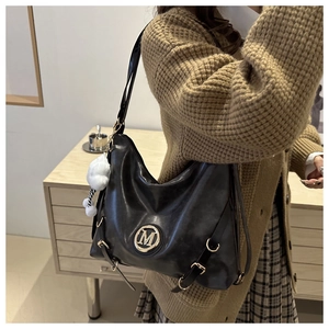 Detail of black tote bag with metallic M logo and plush pompom on a model