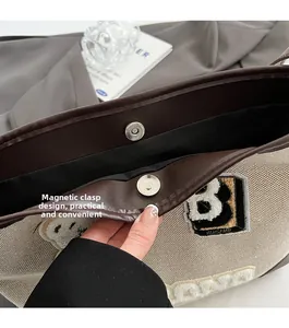 Detail of the magnetic buckle closure on a canvas and leather tote with embroidery