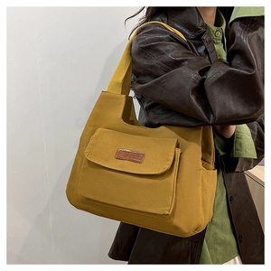 Détail du sac cabas en toile jaune moutarde avec un écusson de mode en cuir à l'avant