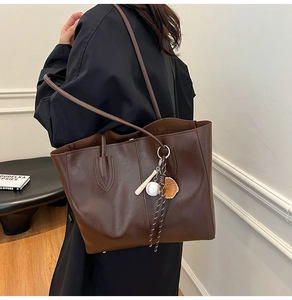 Detailed view of dark brown tote bag featuring a creative baseball theme charm on the strap