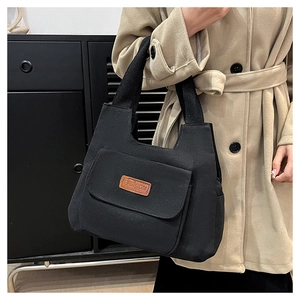 Close-up of black canvas tote bag showing the front pocket with fashion leather label